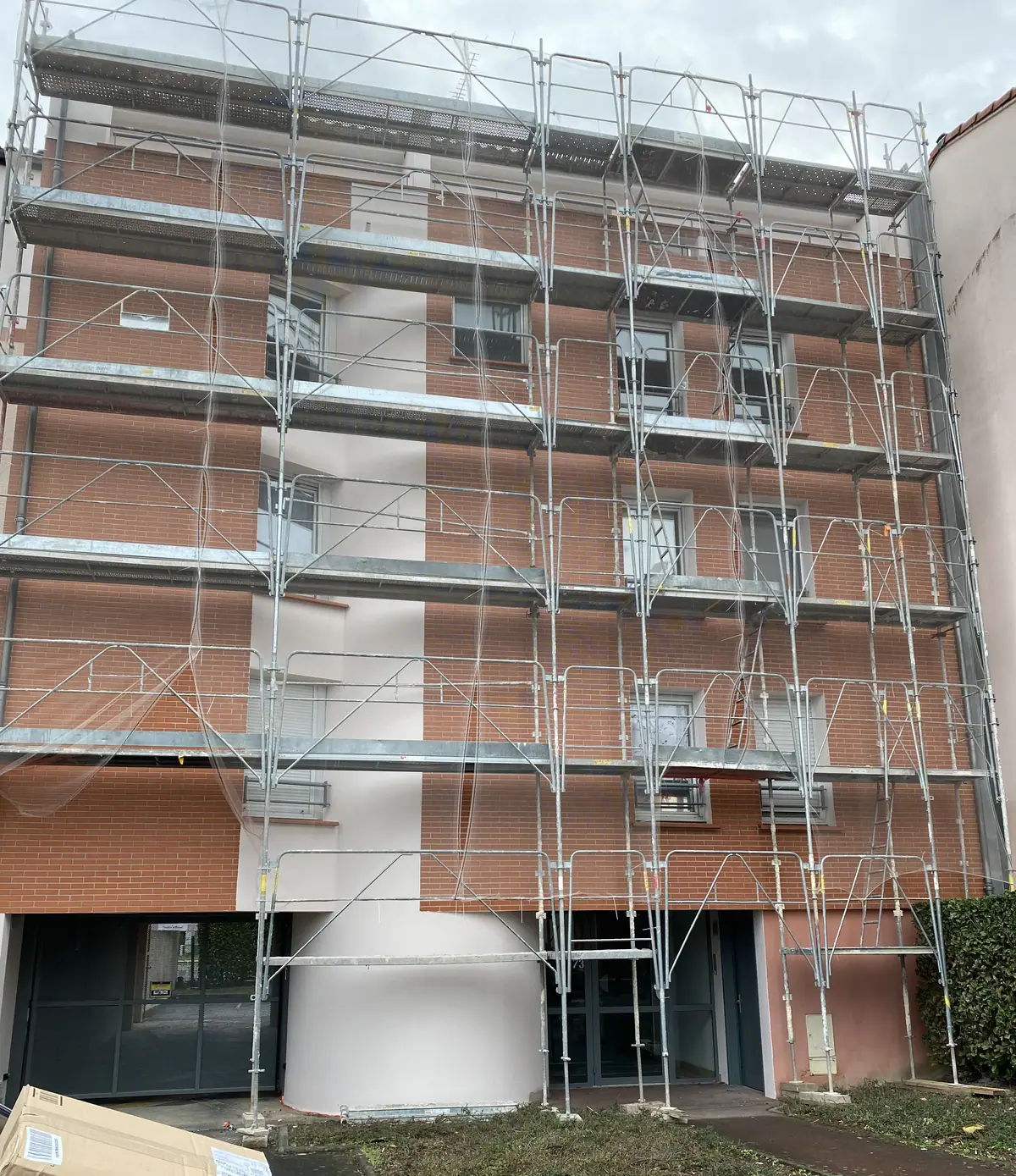 Immeuble en brique rose sous un échafaudage complet, avant ravalement de la façade