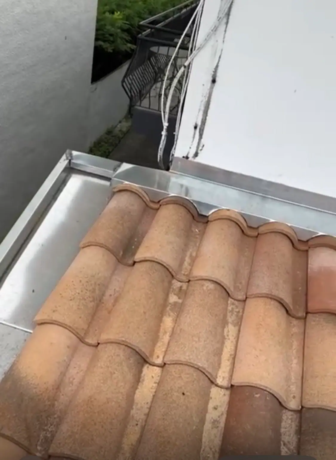 Rive de tuiles romanes posée sur un chéneau en zinc neuf, garde-corps de balcon en arrière-plan