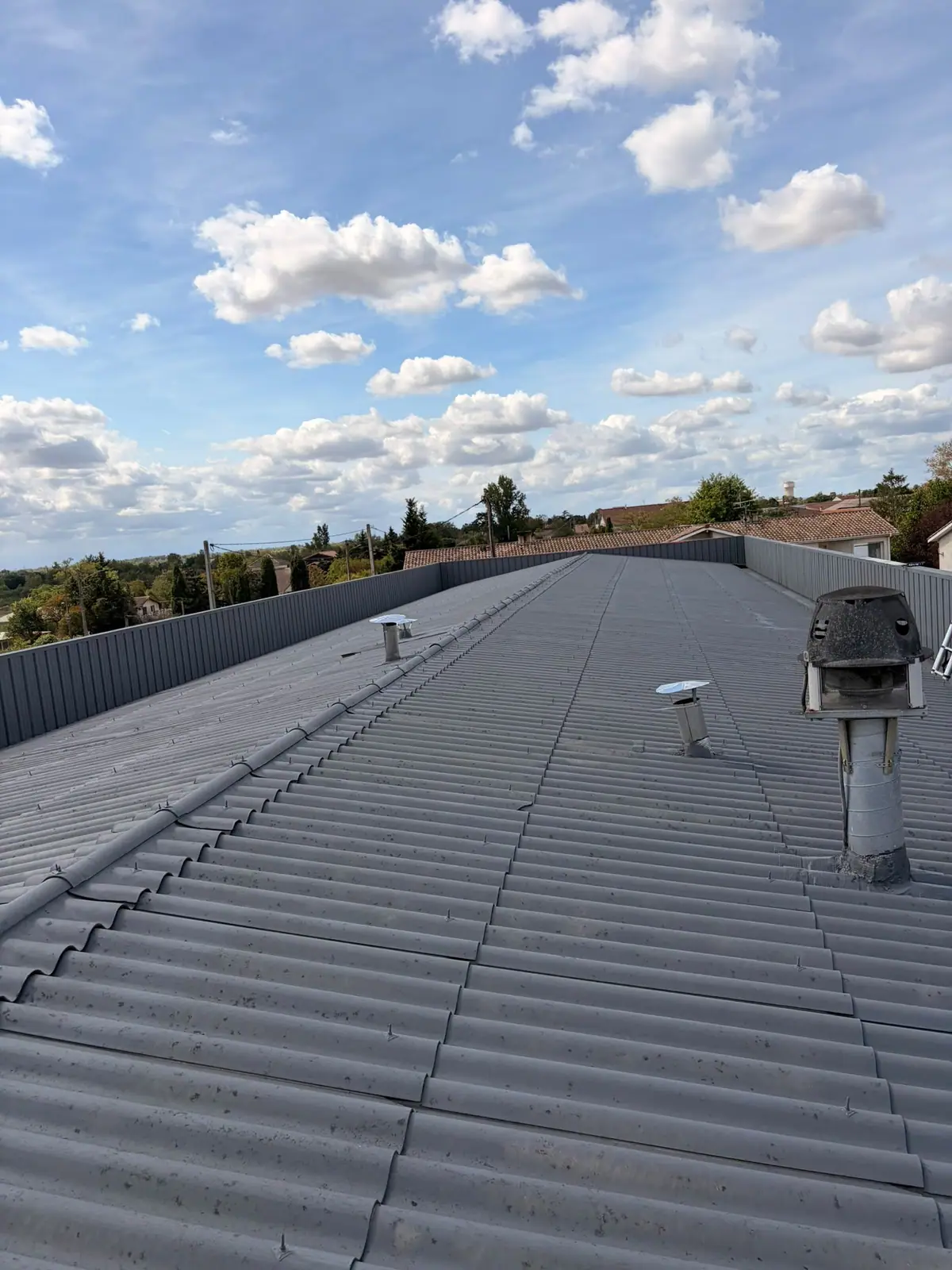 Grande couverture en bac acier gris ondulé avec des sorties de ventilation en inox, sous un ciel de nuages