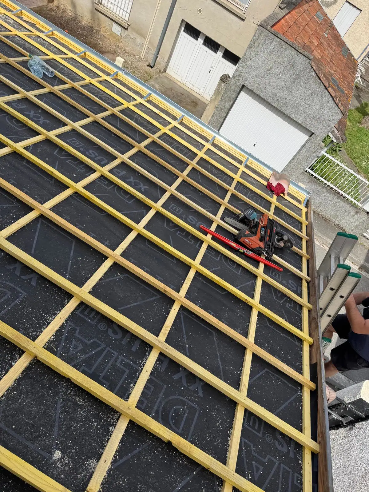 Écran de sous-toiture noir et grille de liteaux et contre-liteaux neufs sur un versant, scie circulaire posée